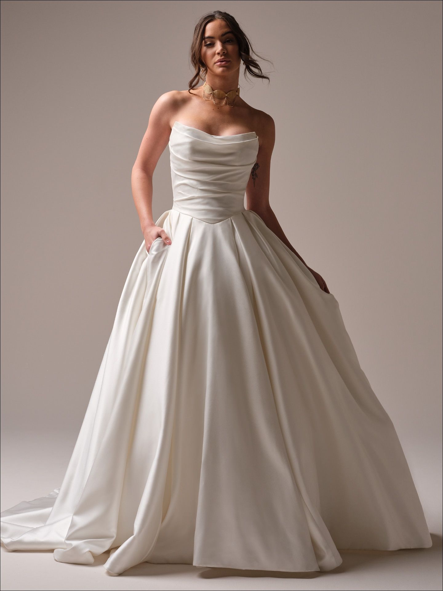 Woman in a strapless ivory ballgown with pockets, posing with hands in pockets.