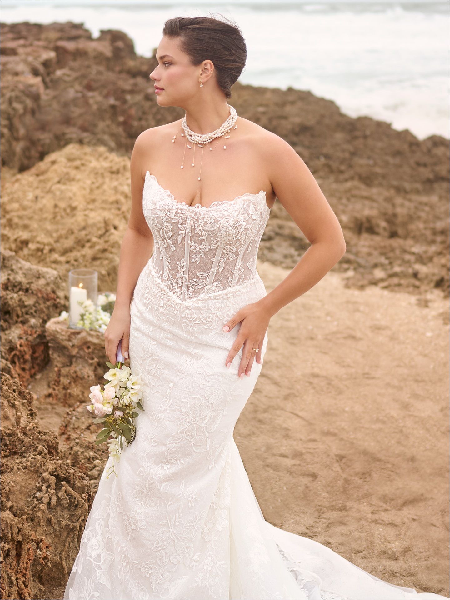 Woman in white wedding dress on beach, holding flowers.