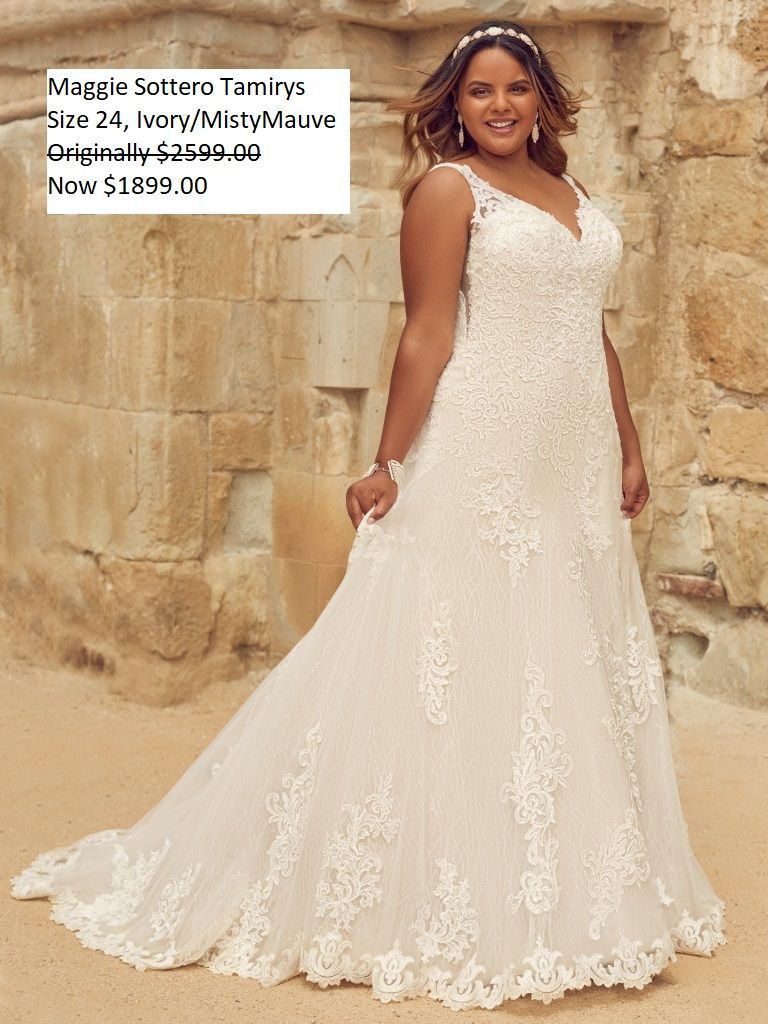 A woman in a white wedding dress is standing in front of a stone wall.