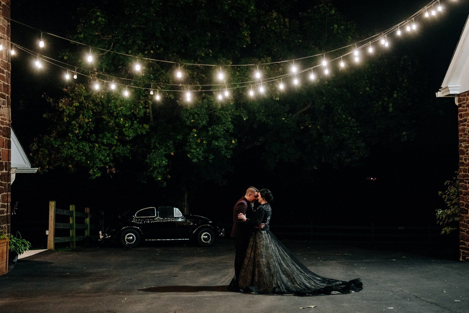 A bride and groom are kissing under a string of lights.
