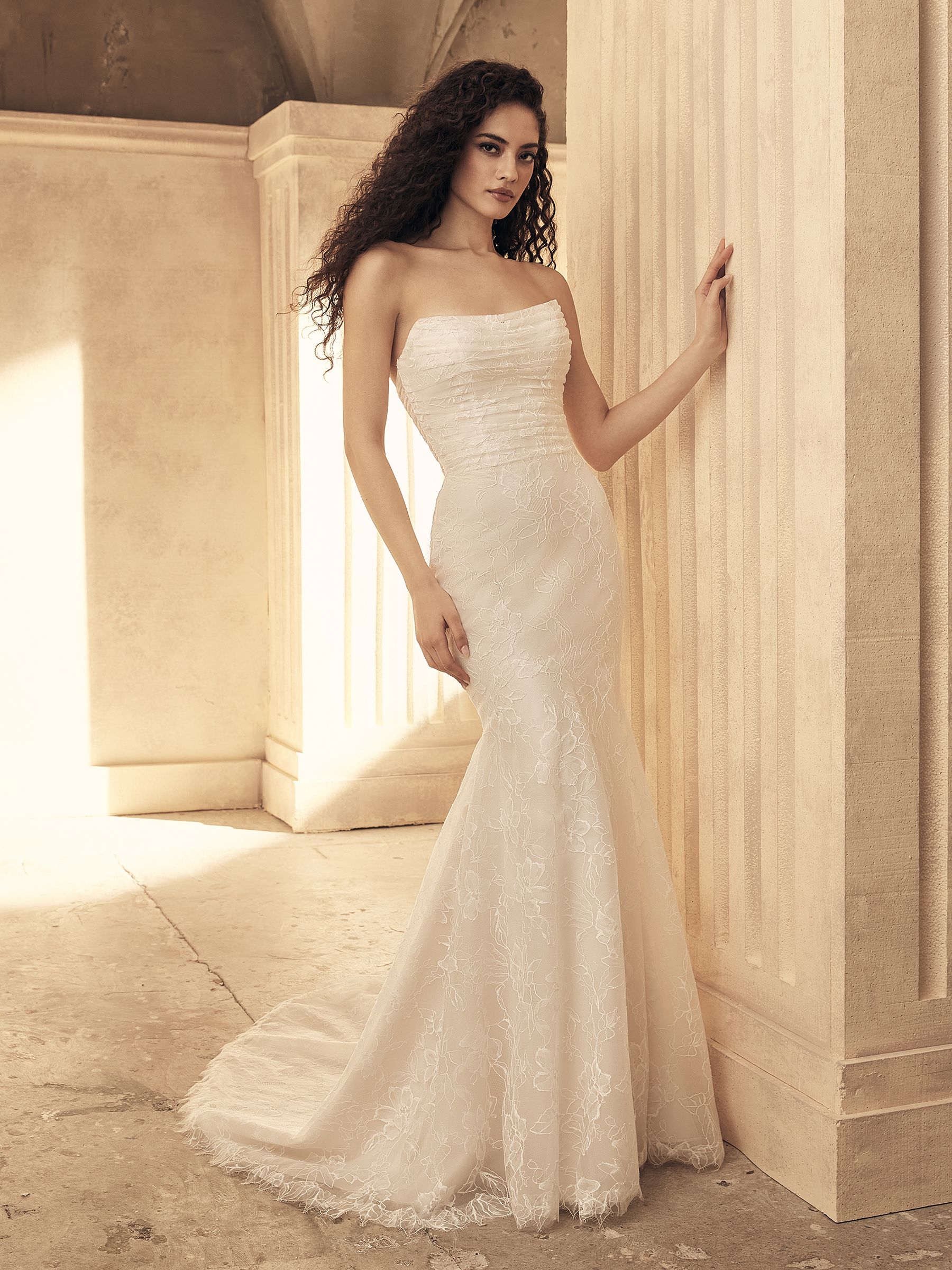 Woman in a strapless white wedding dress leans against a column, in a stone archway.