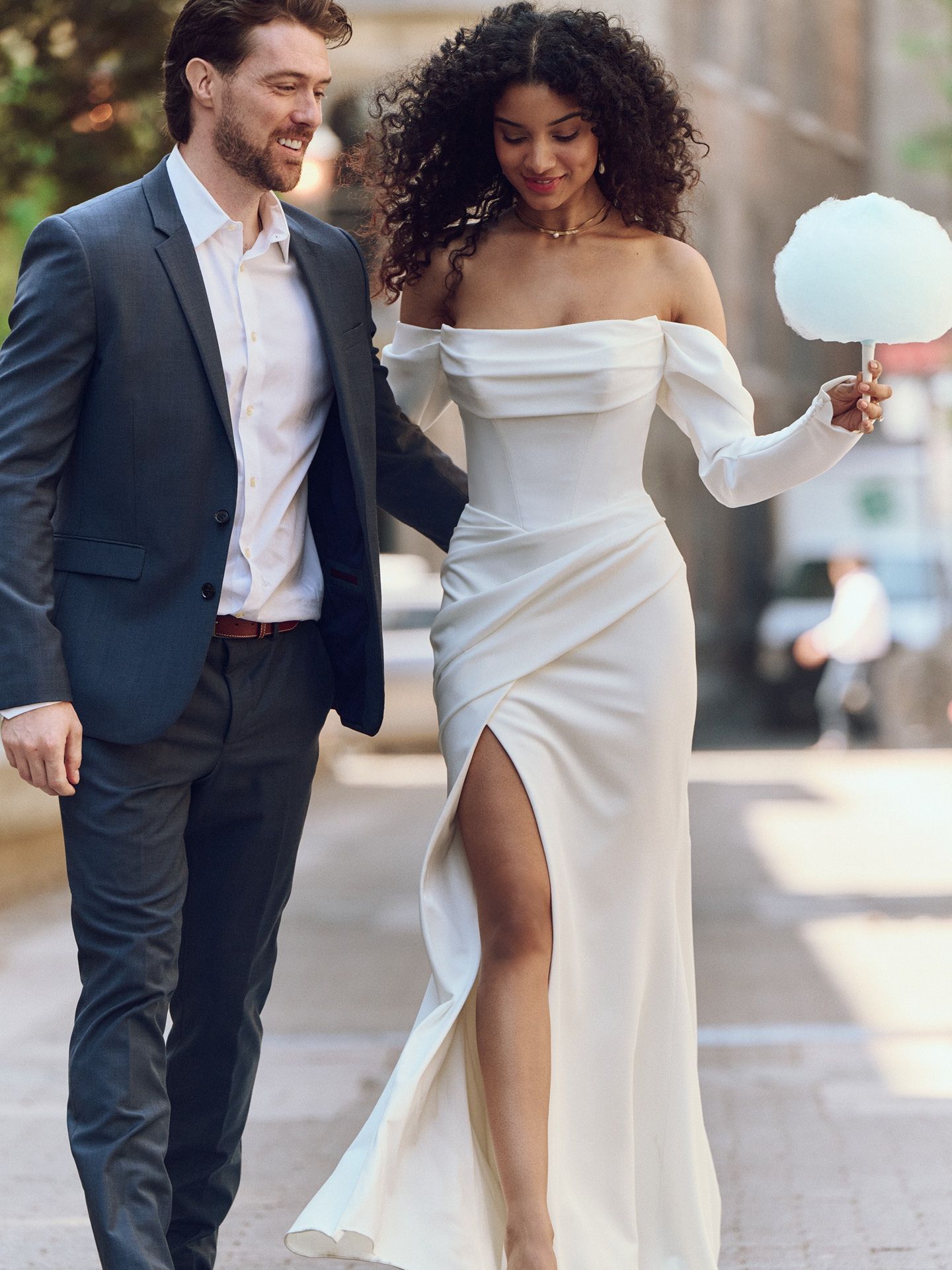 Couple walking down a city street, the woman in a white gown holding cotton candy.