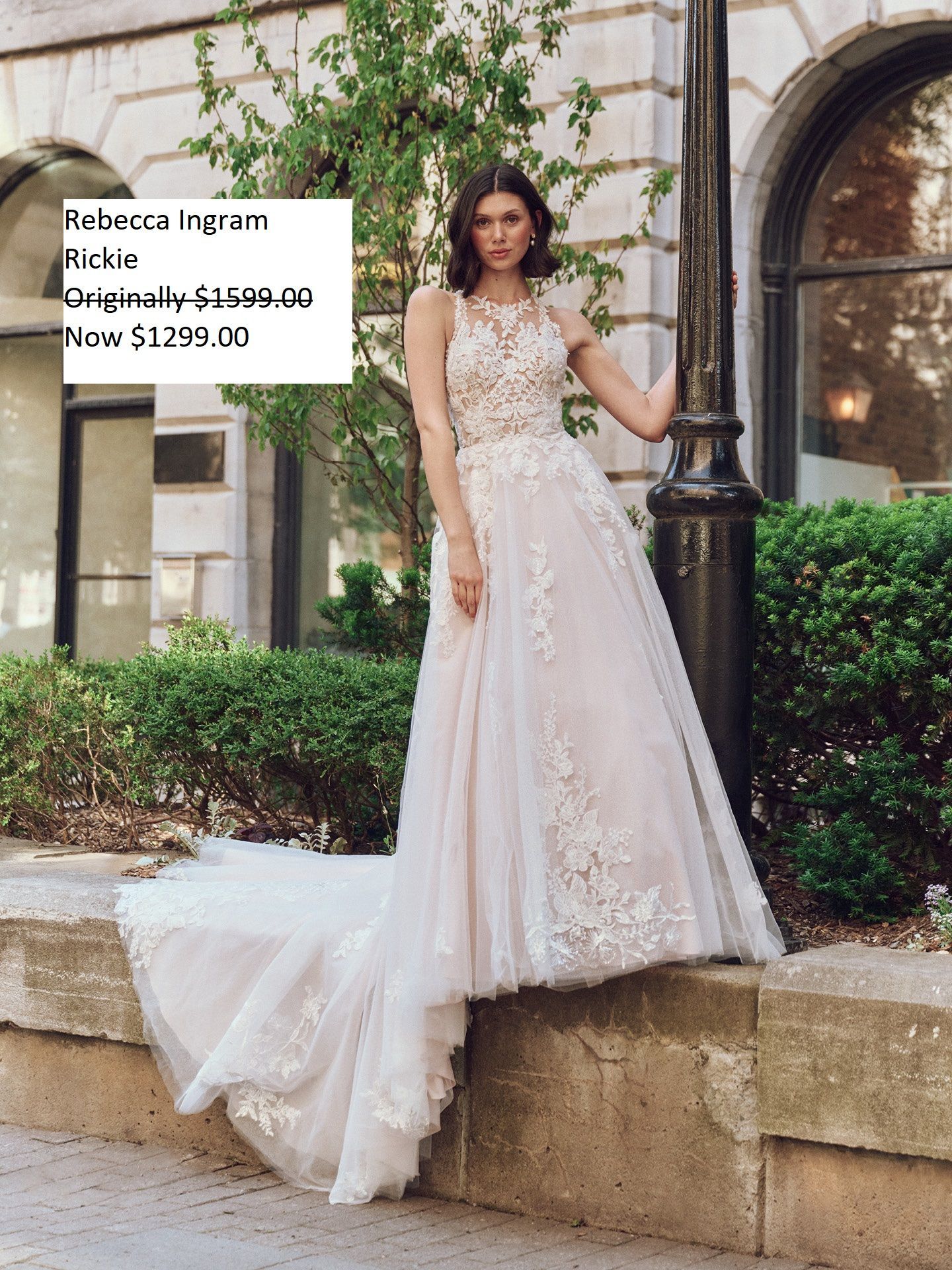 Woman in wedding dress, standing outdoors. Dress is white with lace detailing; building and greenery in background. Maggie Sottero Rickie