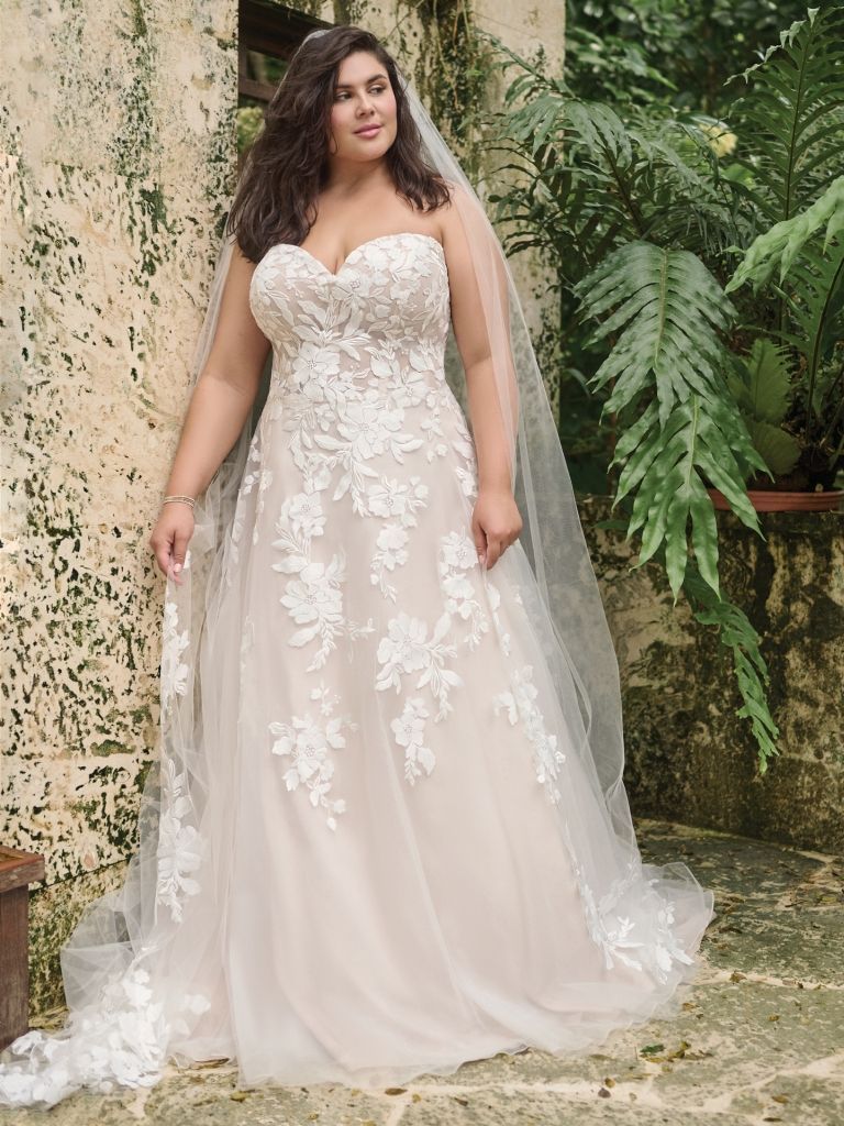 A plus size bride is wearing a wedding dress and veil.