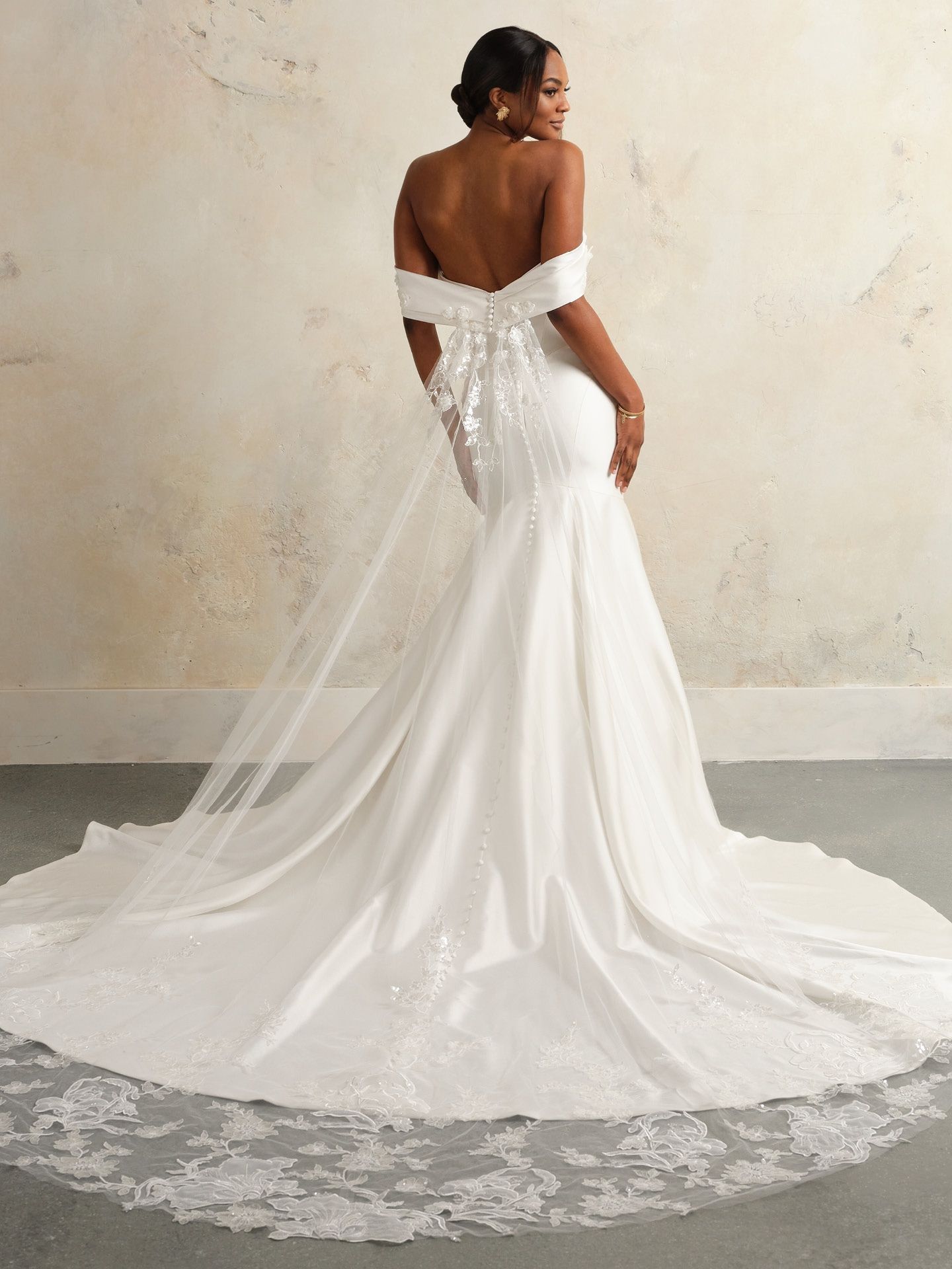 Bride in an off-the-shoulder white wedding dress with a long train, facing away.