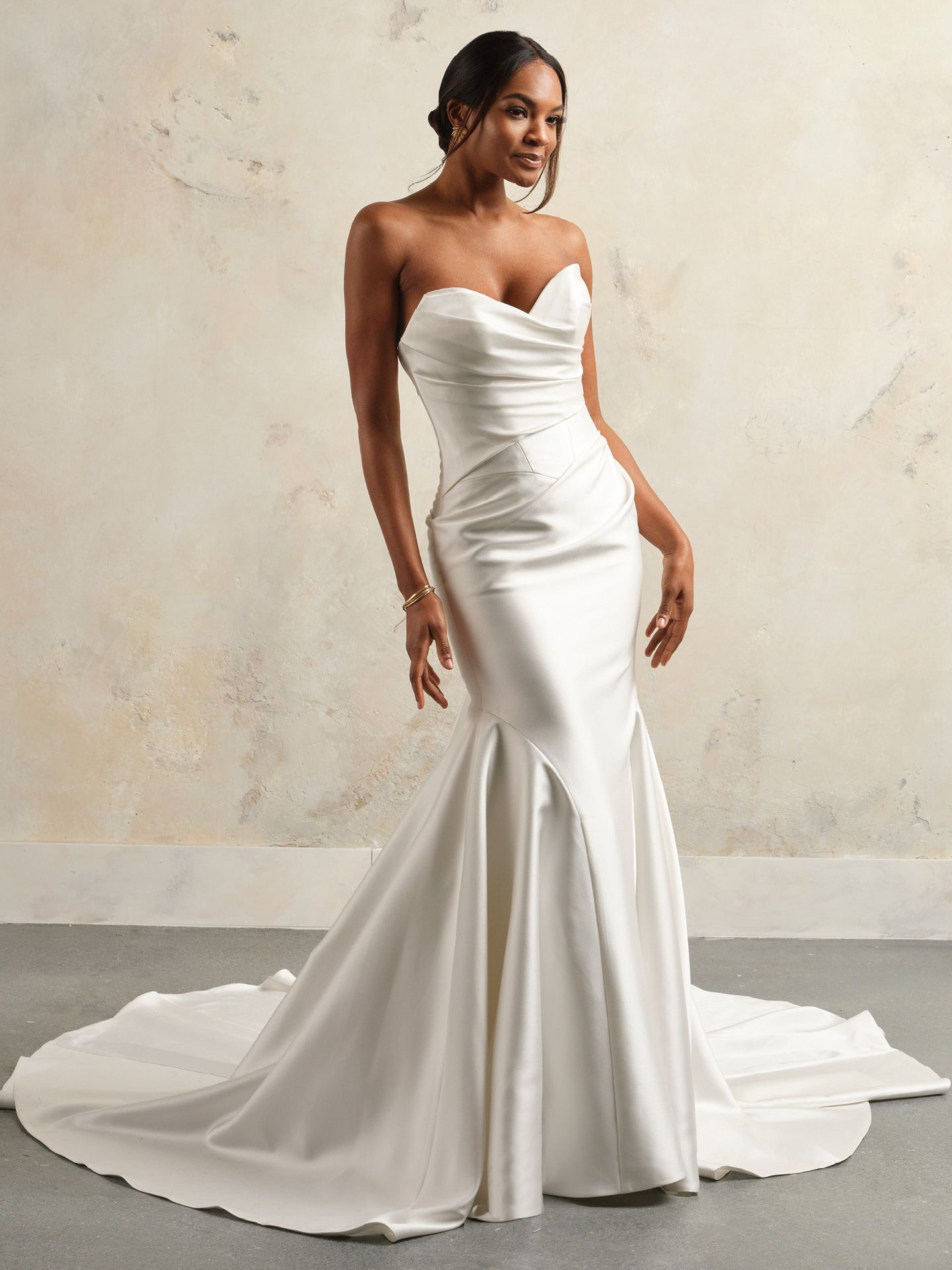 Woman in a white strapless mermaid-style wedding gown, posing against a neutral backdrop.