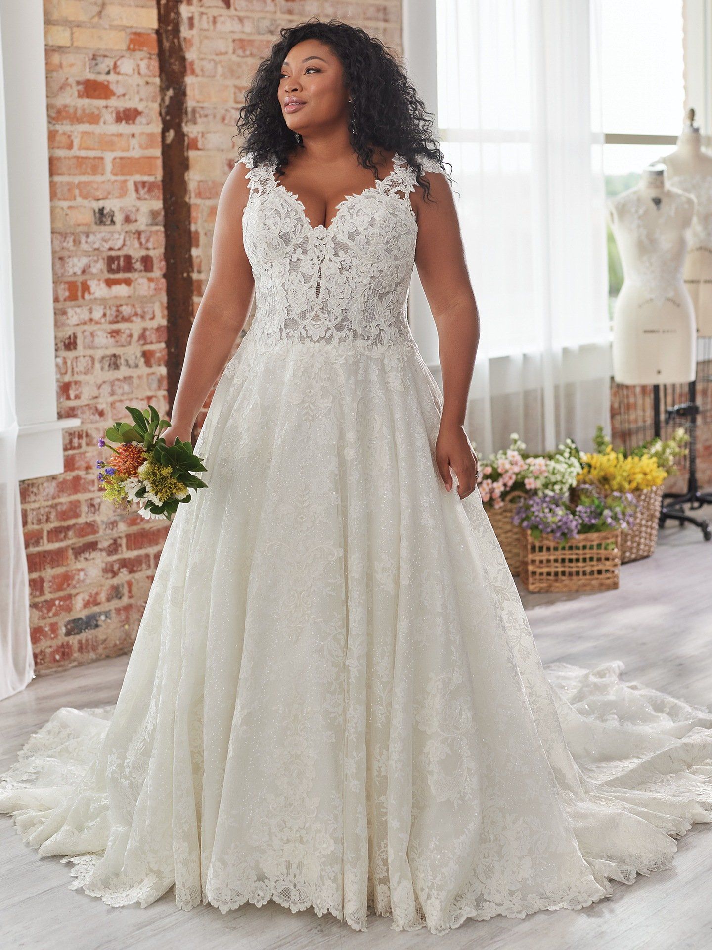 A plus size bride is wearing a white wedding dress and holding a bouquet of flowers.