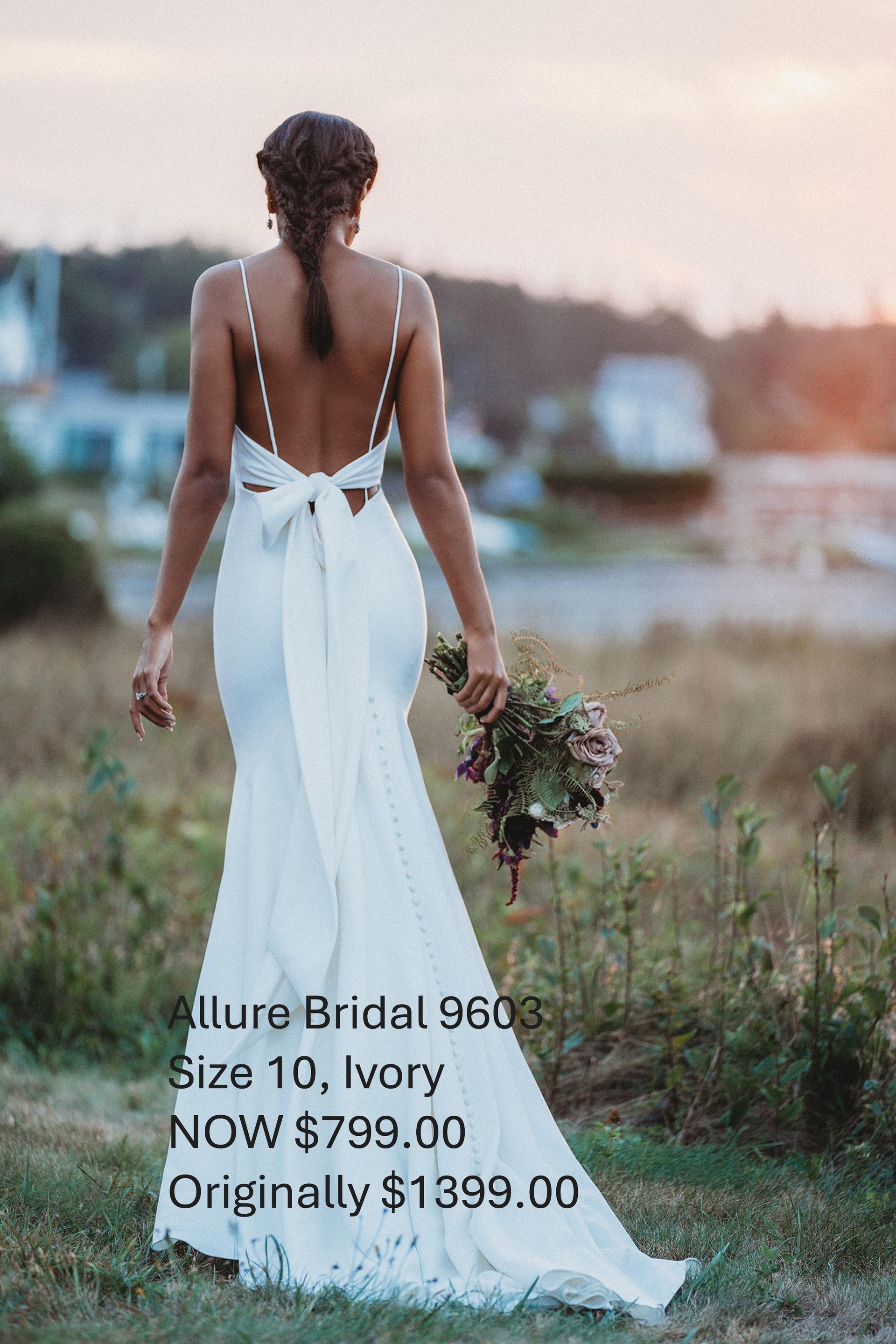 A woman in a white wedding dress is standing in a field holding a bouquet of flowers.