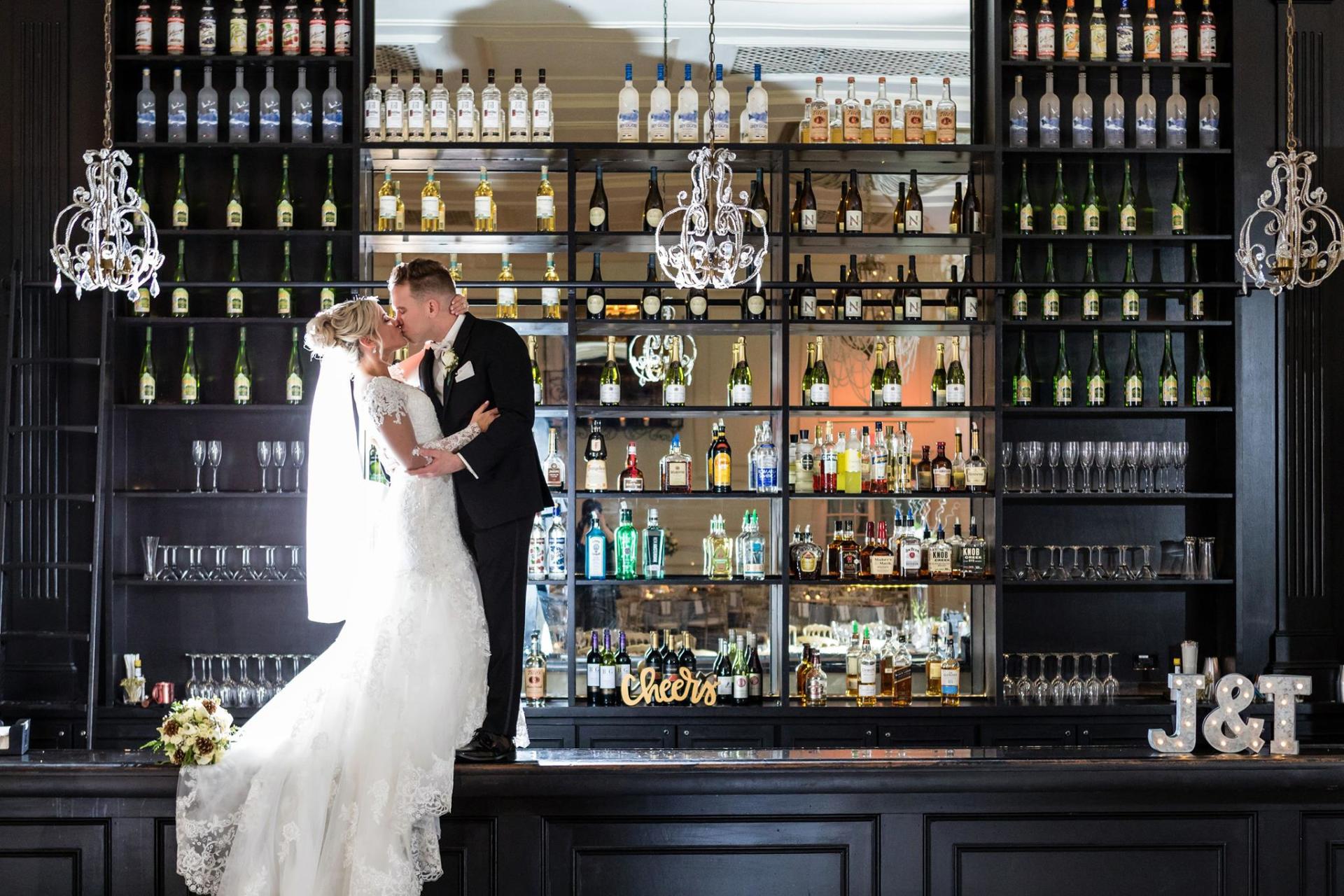 A bride and groom are kissing in front of a bar.