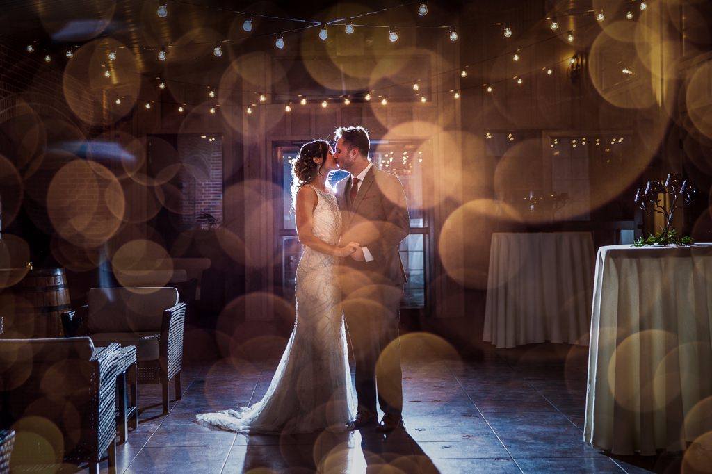 A bride and groom are kissing in a room with lights on the ceiling.
