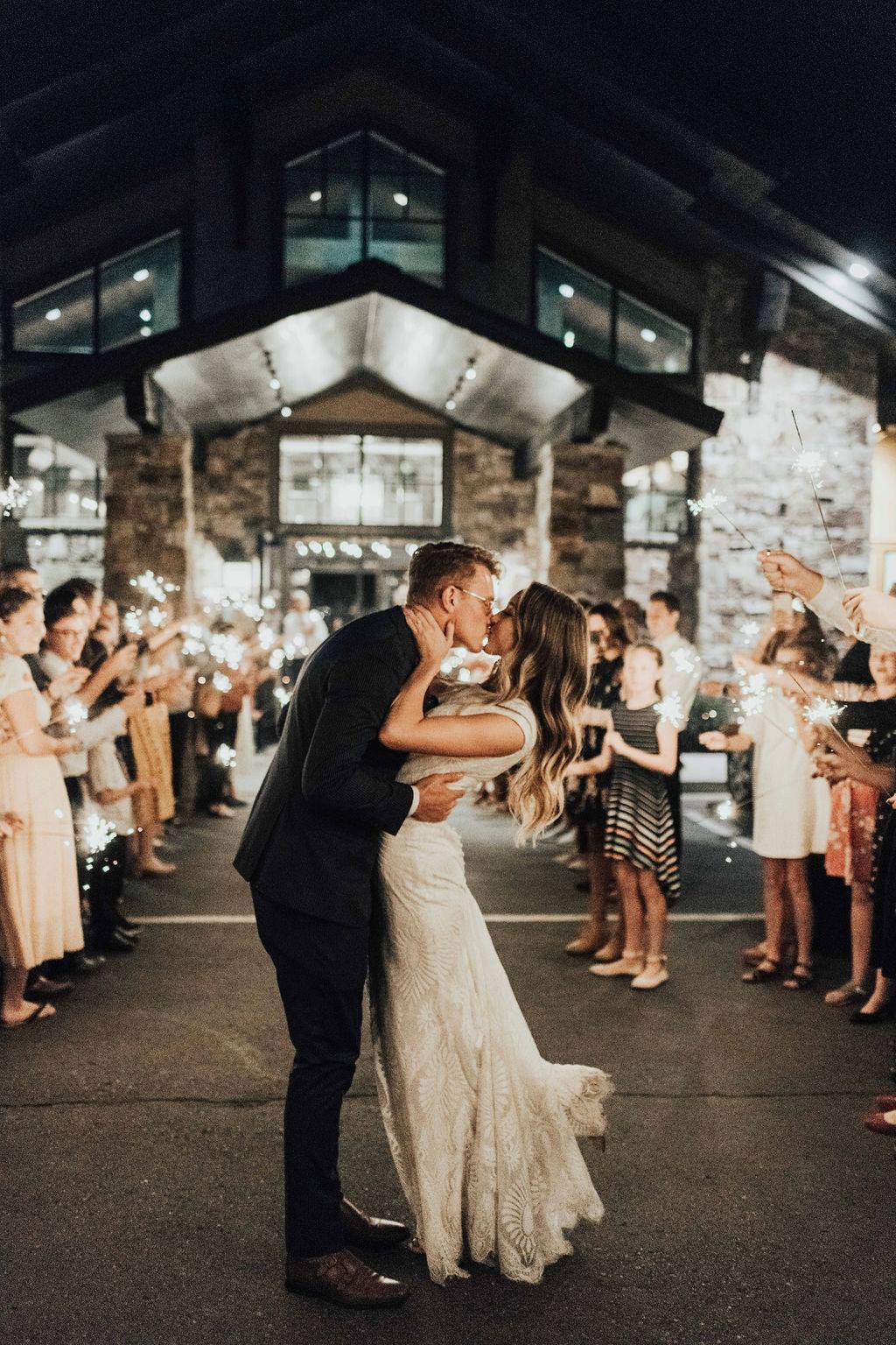 A bride and groom kissing in front of a crowd of people holding sparklers.