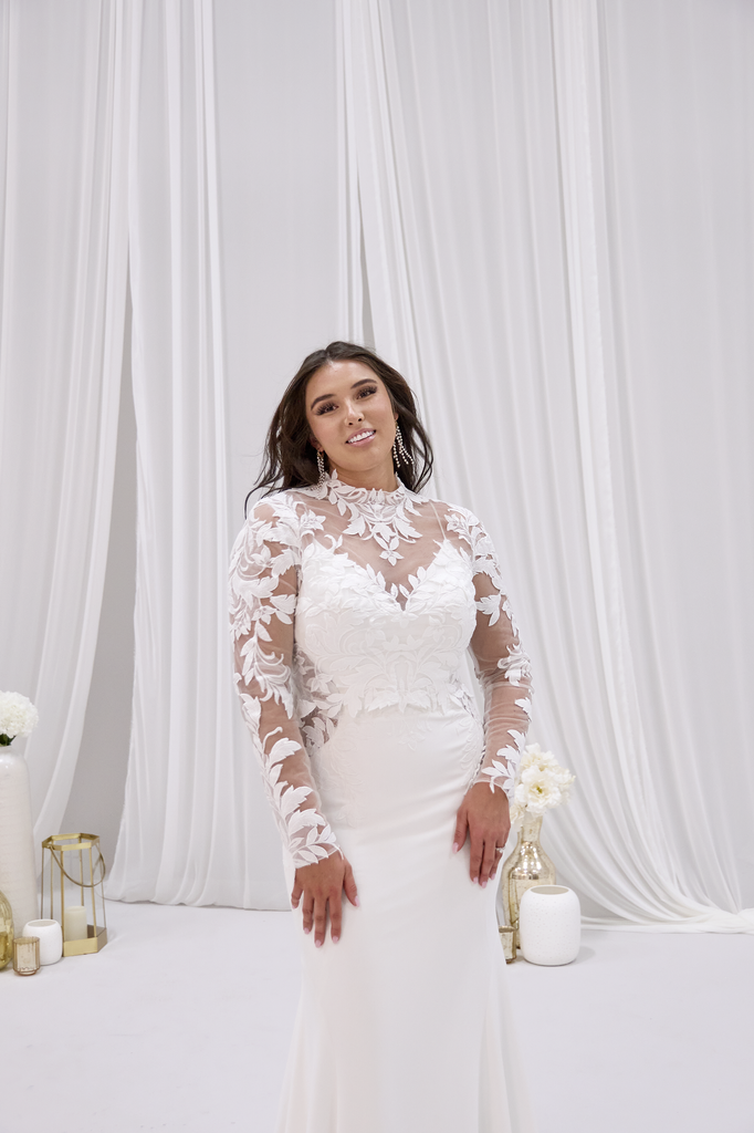 A woman in a wedding dress is standing in front of a wall.