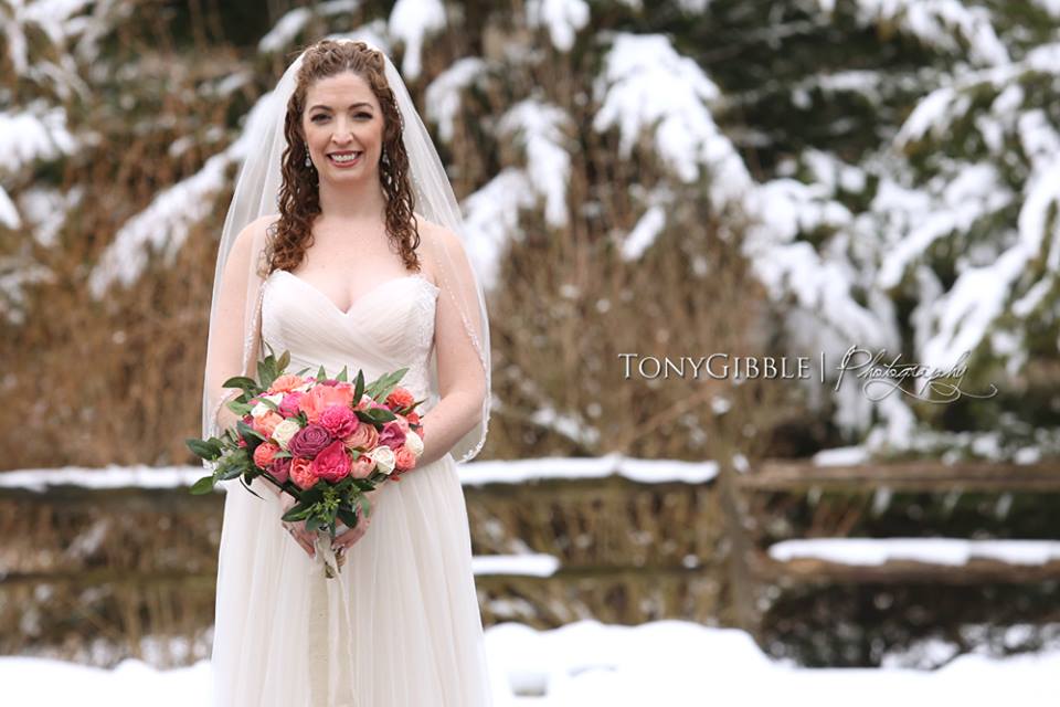 A bride in a wedding dress is standing in the snow holding a bouquet of flowers.