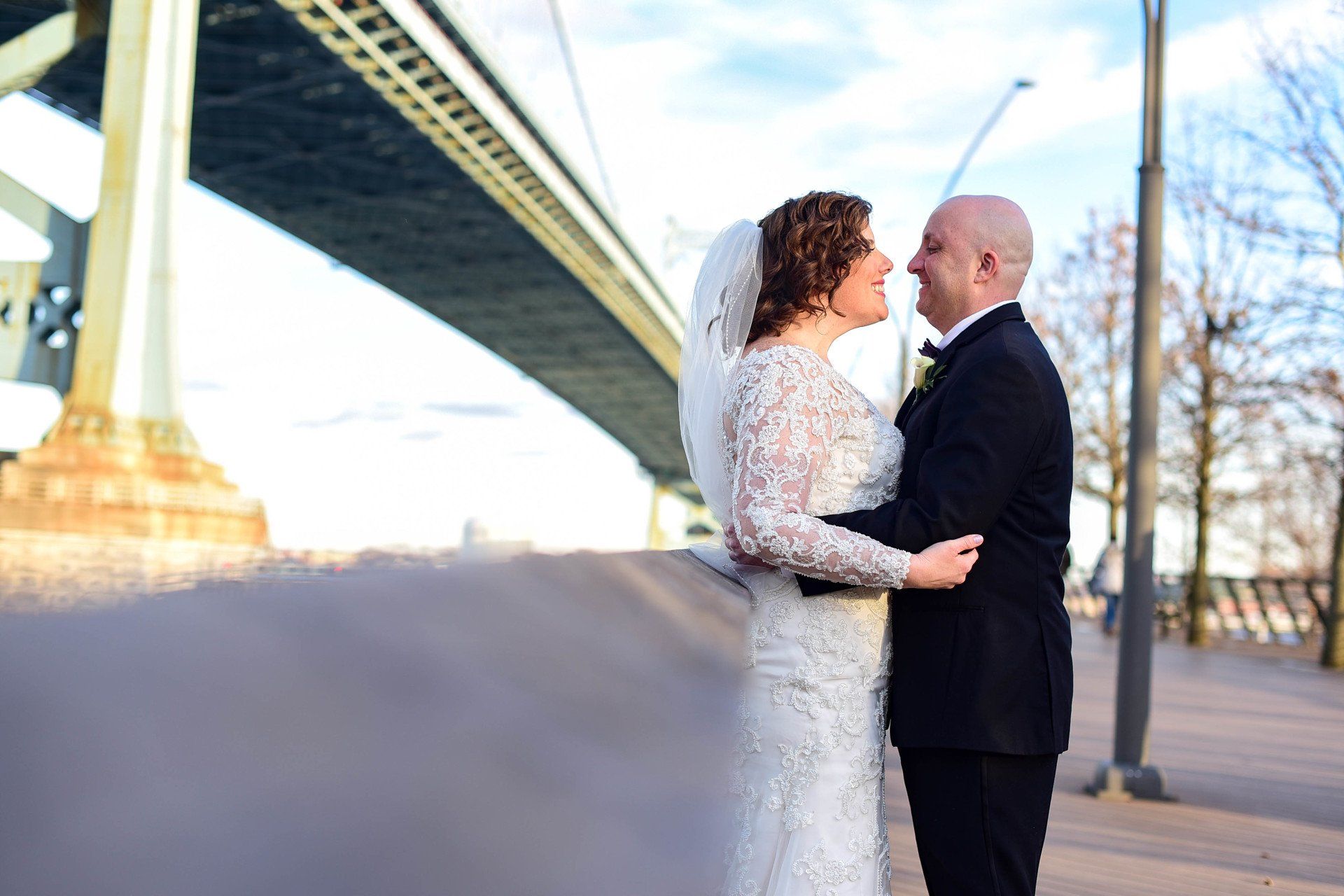 A bride and groom are kissing in front of a bridge.