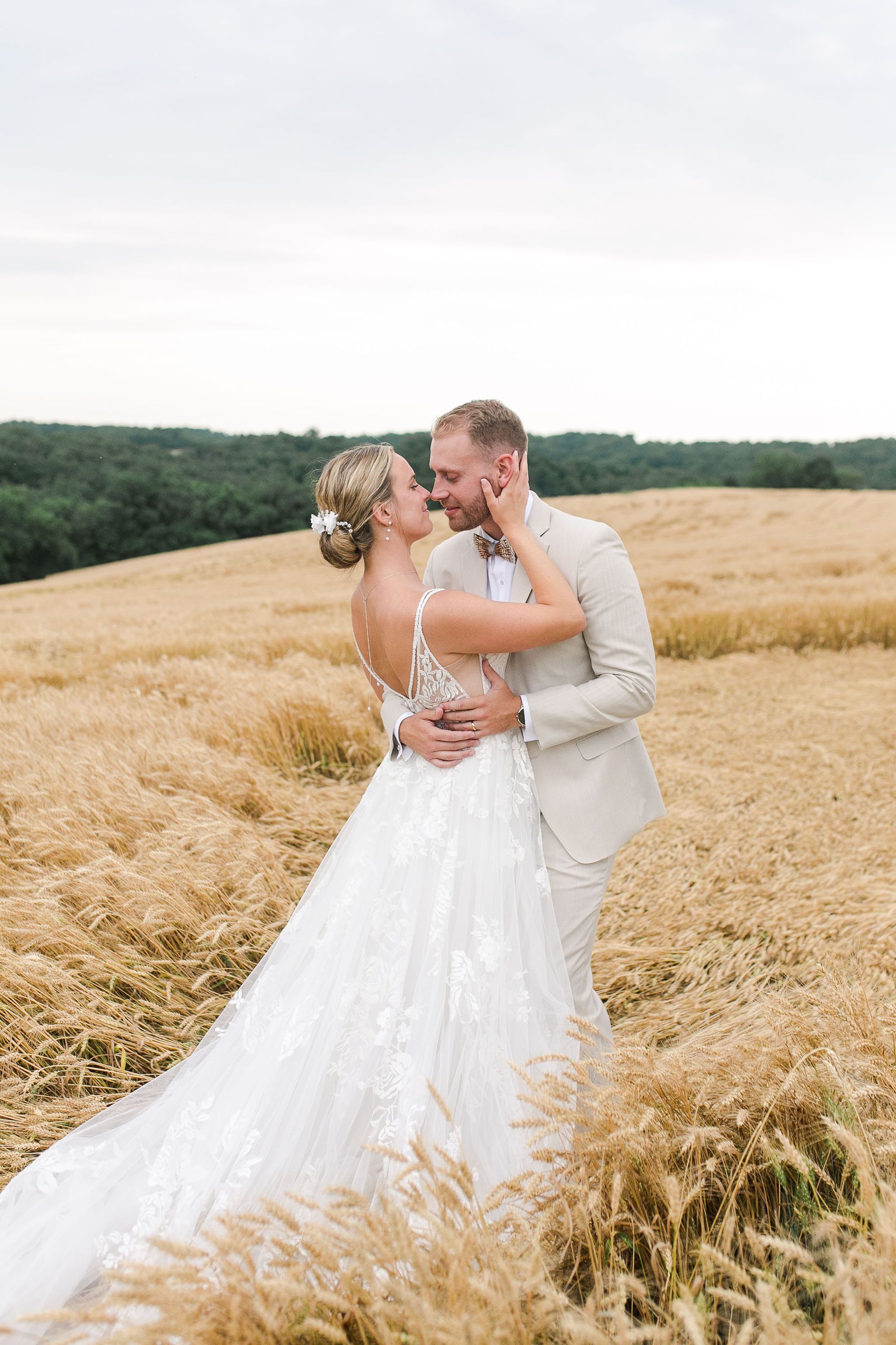 Bride and groom embrace in a golden wheat field. The bride wears a white dress, the groom a beige suit.