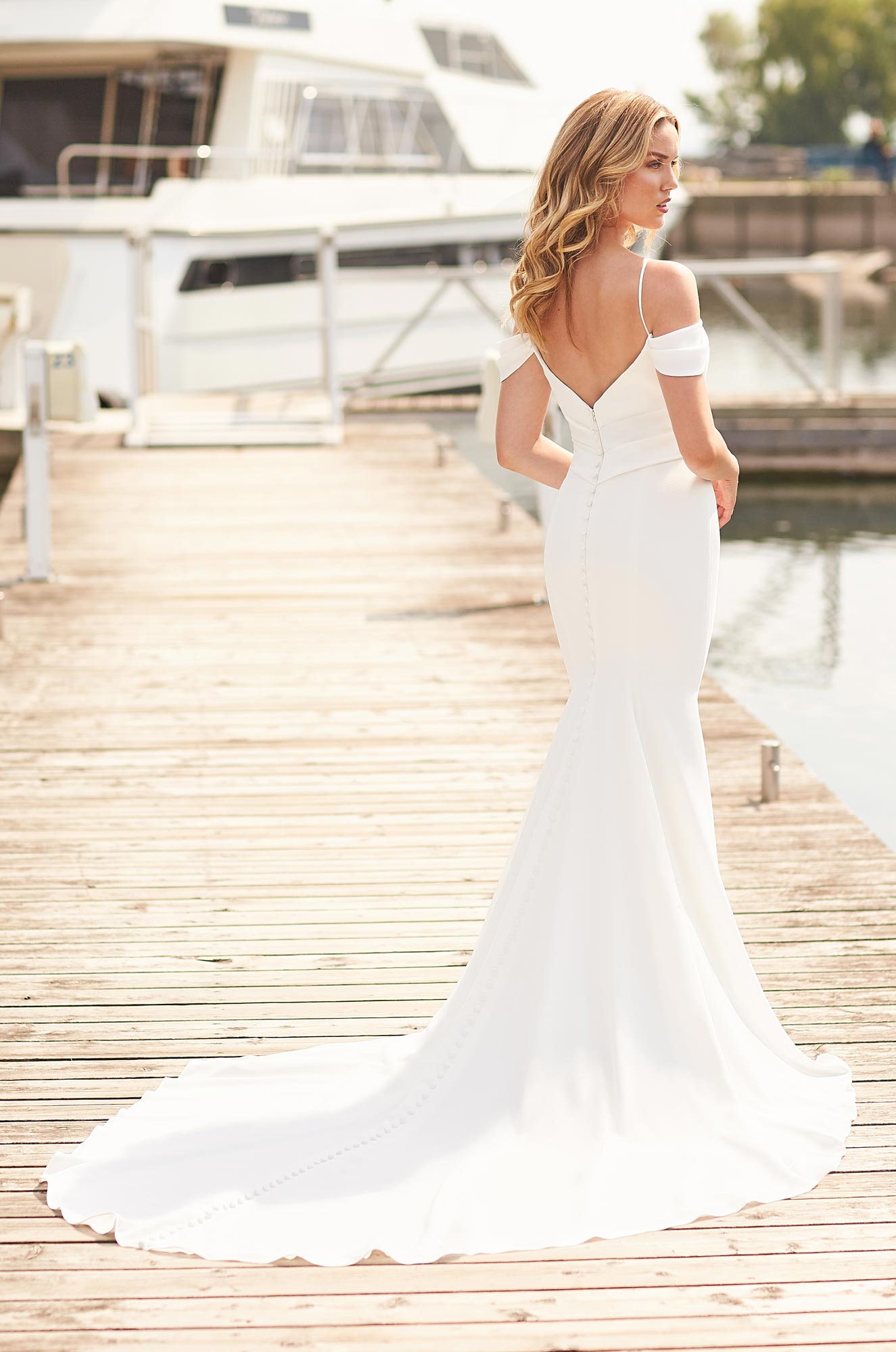 A woman in a white wedding dress is standing on a dock next to a boat.