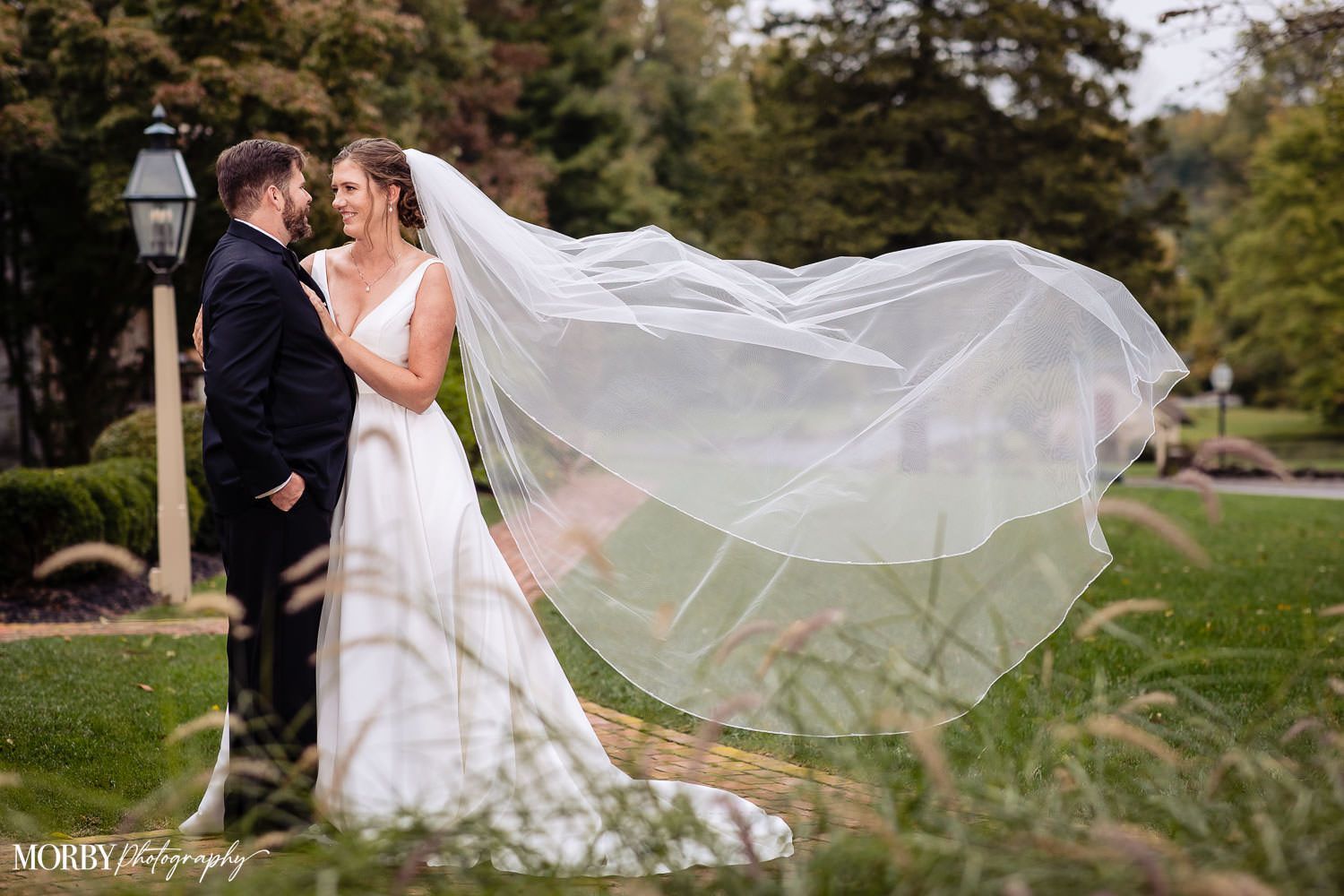A bride and groom are posing for a picture with their veil blowing in the wind.