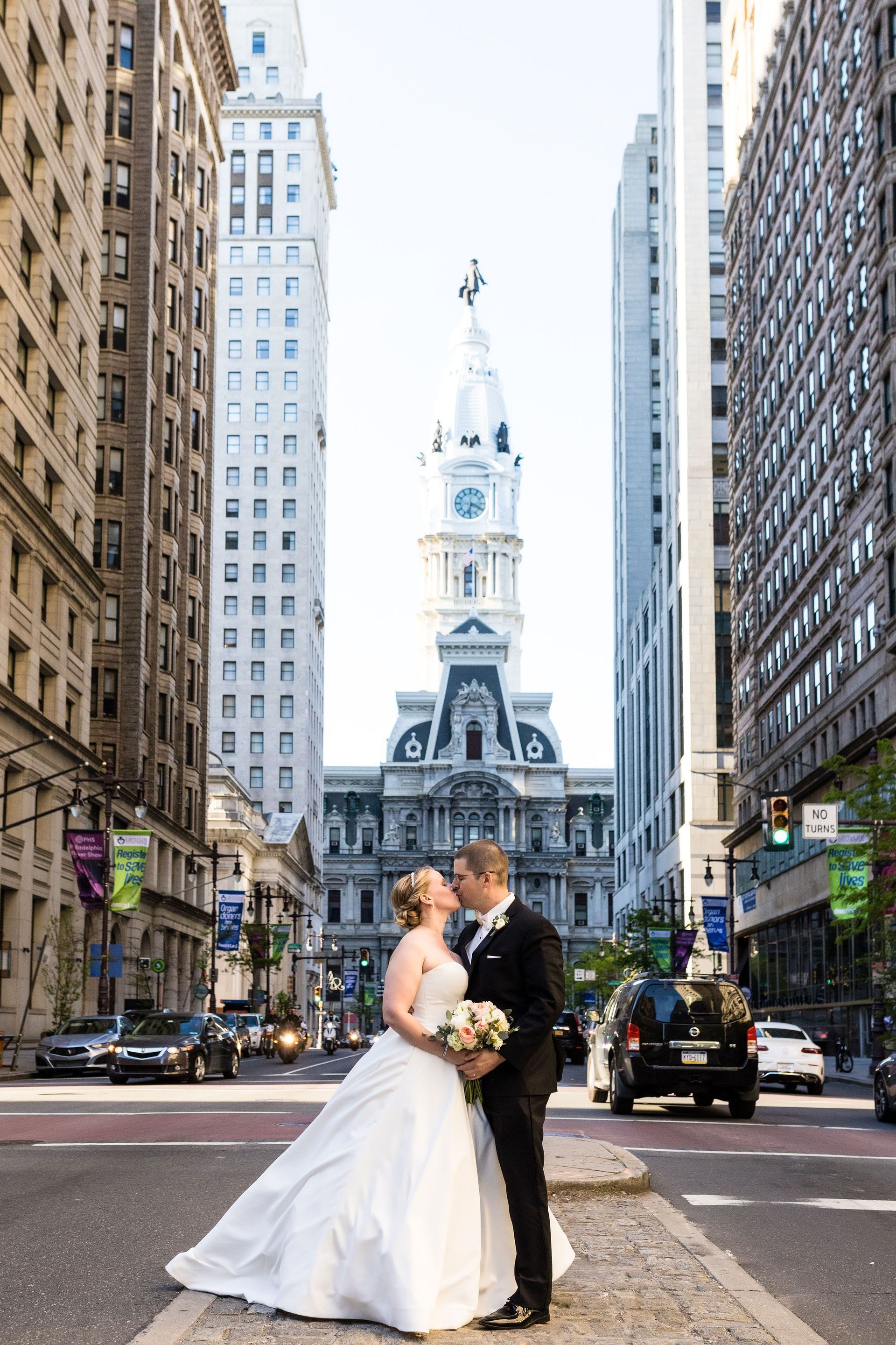 A bride and groom are kissing in front of a large building in a city.