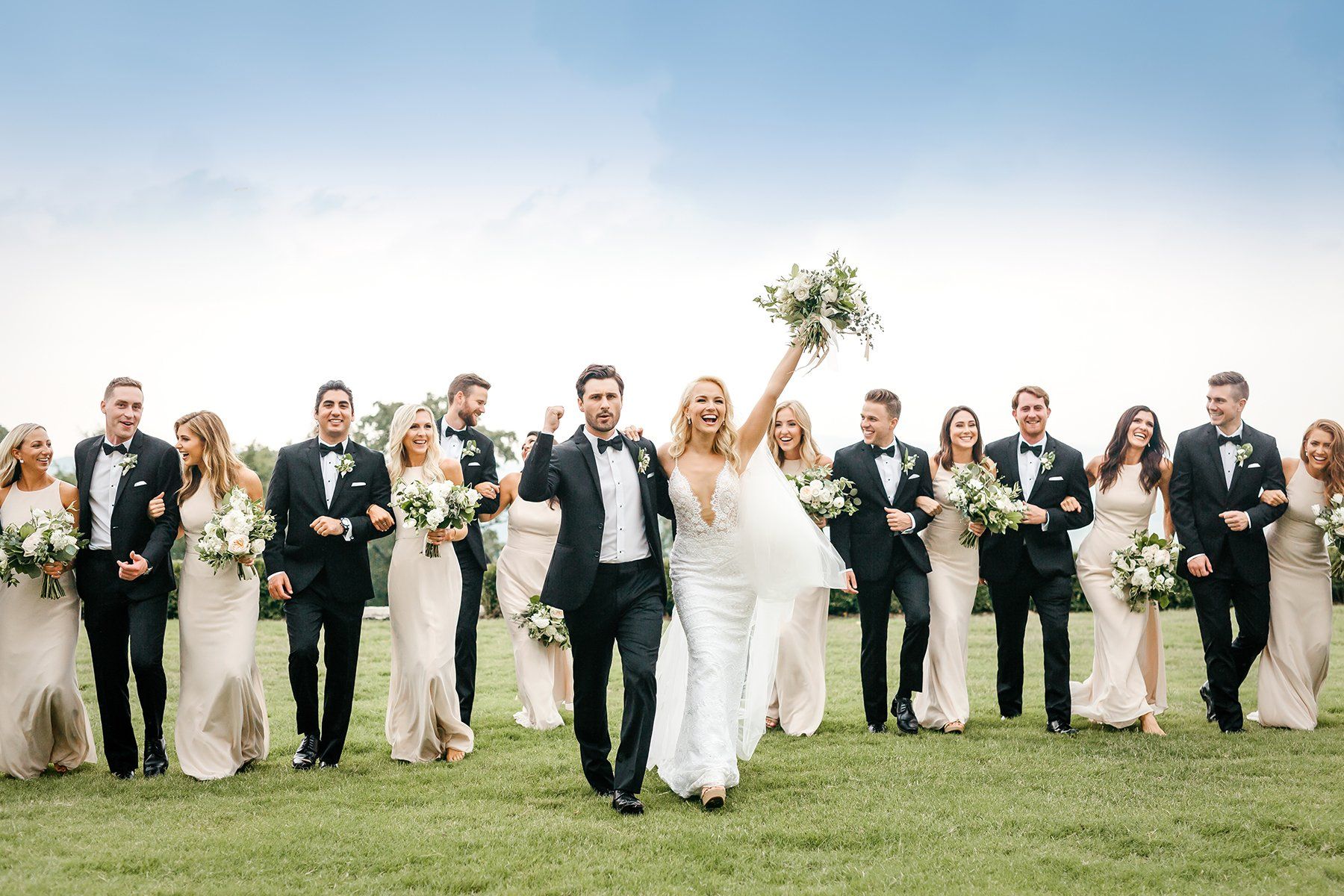 A bride and groom are walking with their wedding party in a field.