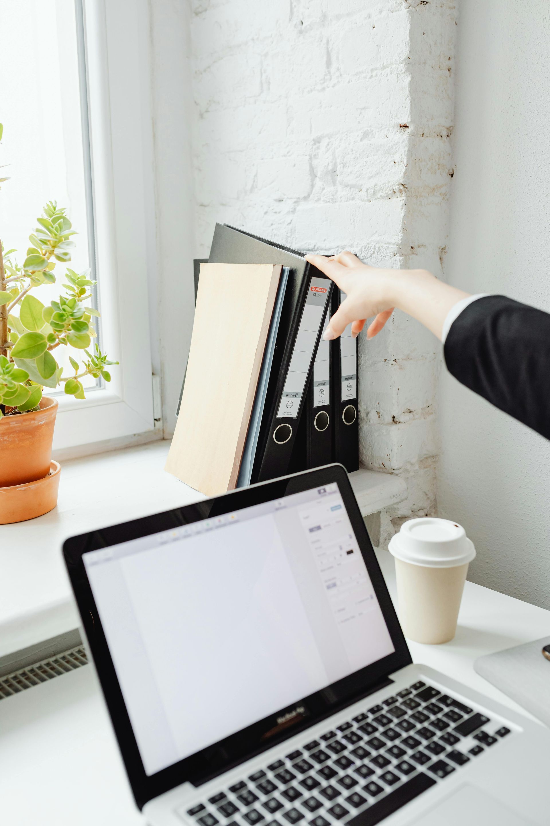 A person is pointing at a laptop computer on a desk.