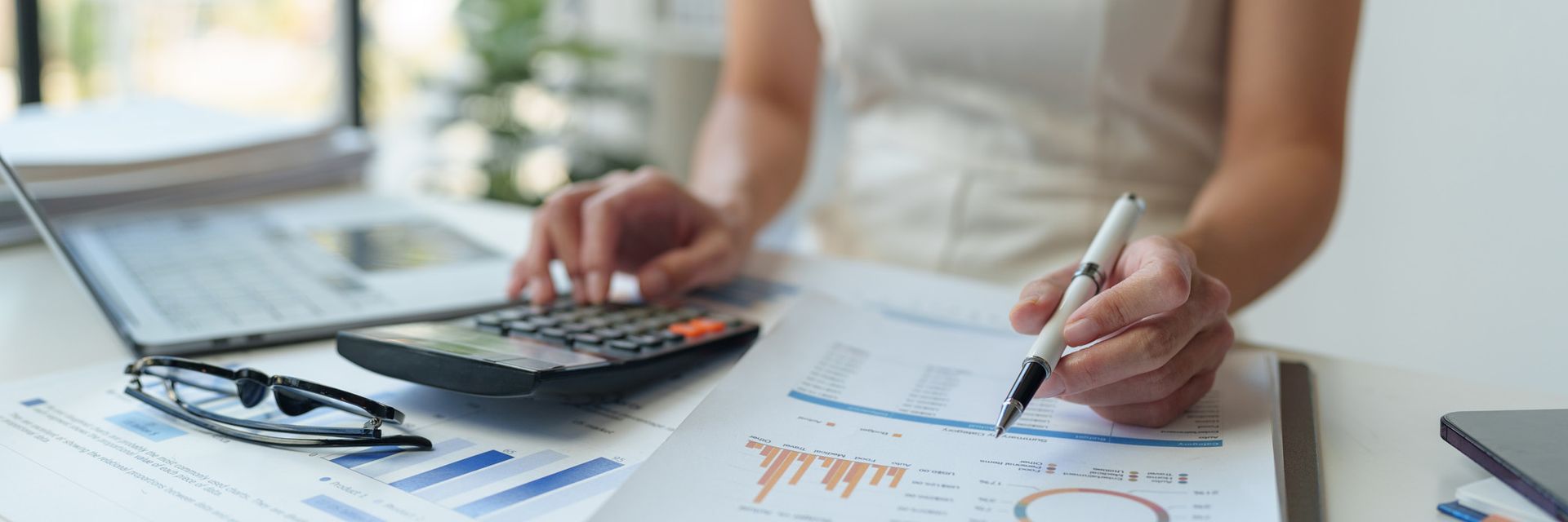 A woman is sitting at a desk using a calculator and a pen.