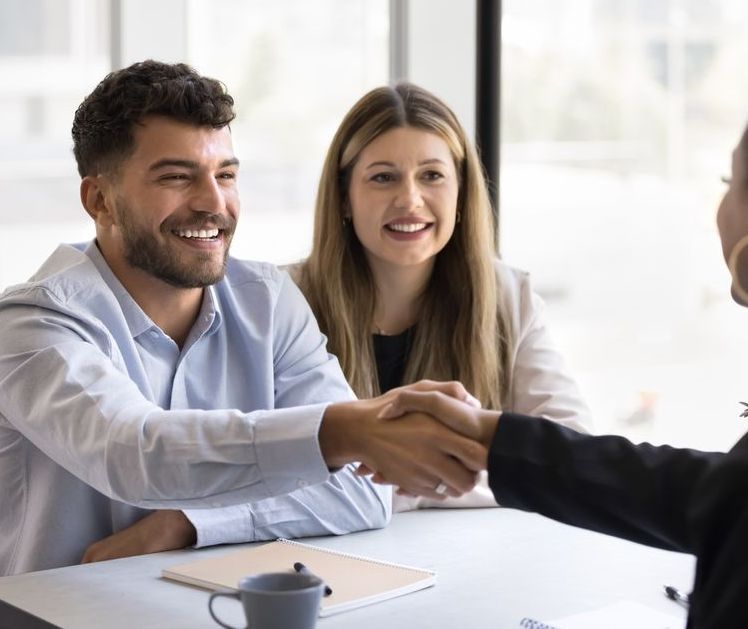 A man and a woman are shaking hands at a table.