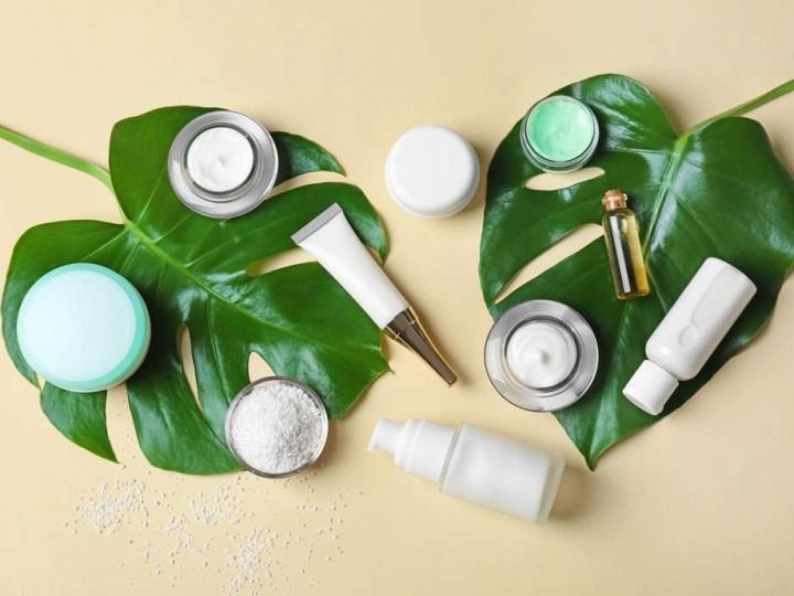 Skincare products arranged on and around tropical leaves, on a beige background.