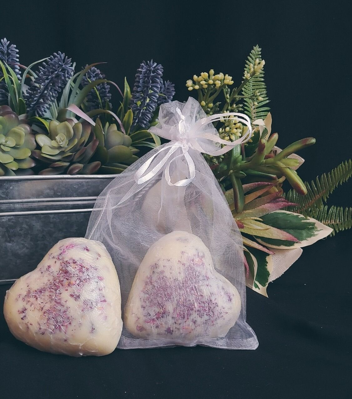 Heart-shaped soaps with purple sprinkles in a sheer bag, next to faux plants in a metal container.