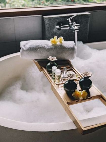 Bubbling bathtub with wooden tray holding spa products, towels, and yellow flowers.