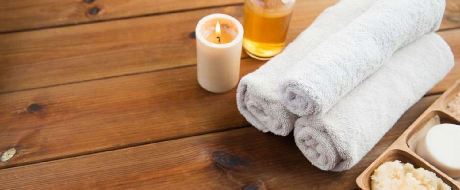 Spa setting: towels, candle, oil, and soap on a wooden surface.