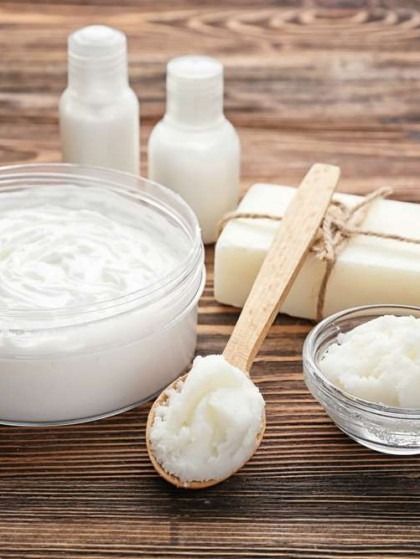 Jar and spoon filled with white cream, bottles, and soap on wood table.