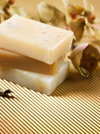 Three bars of soap stacked on gold-striped surface, with dried flowers in the background.