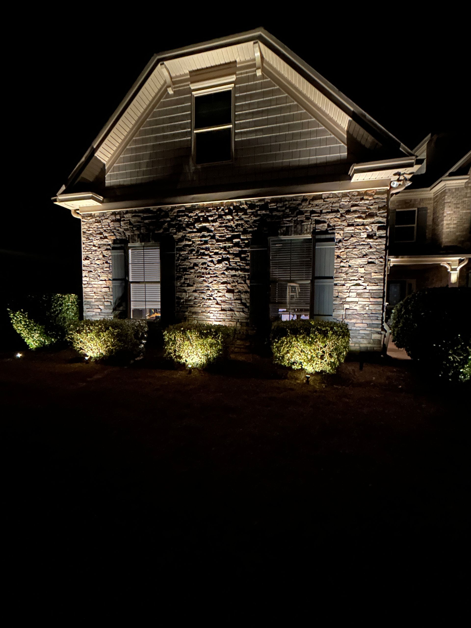 Night view of a house with stone facade, illuminated by landscape lighting.