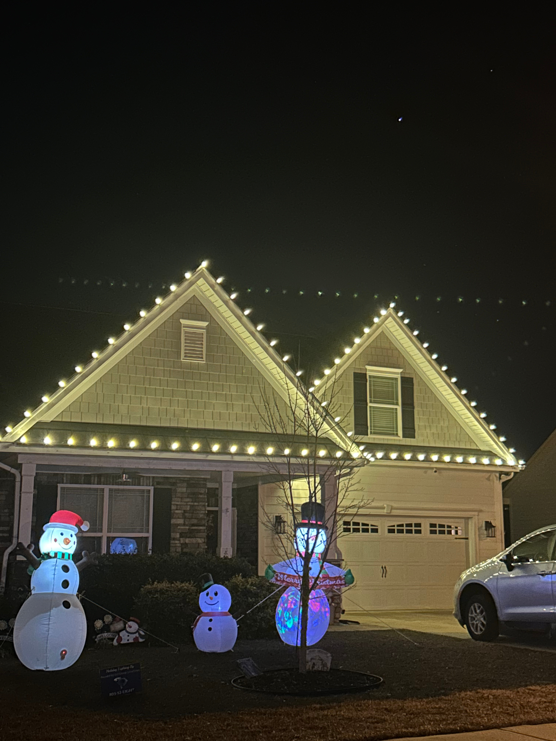 House with Christmas lights and inflatable snowmen at night.