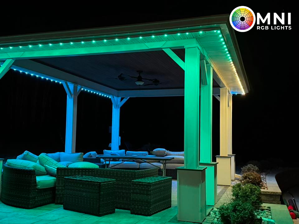 Gazebo lit with teal and blue RGB lights at night. Cushioned outdoor furniture visible.