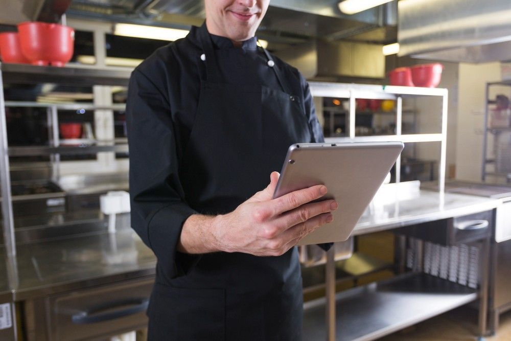 A chef is holding a tablet in a kitchen.