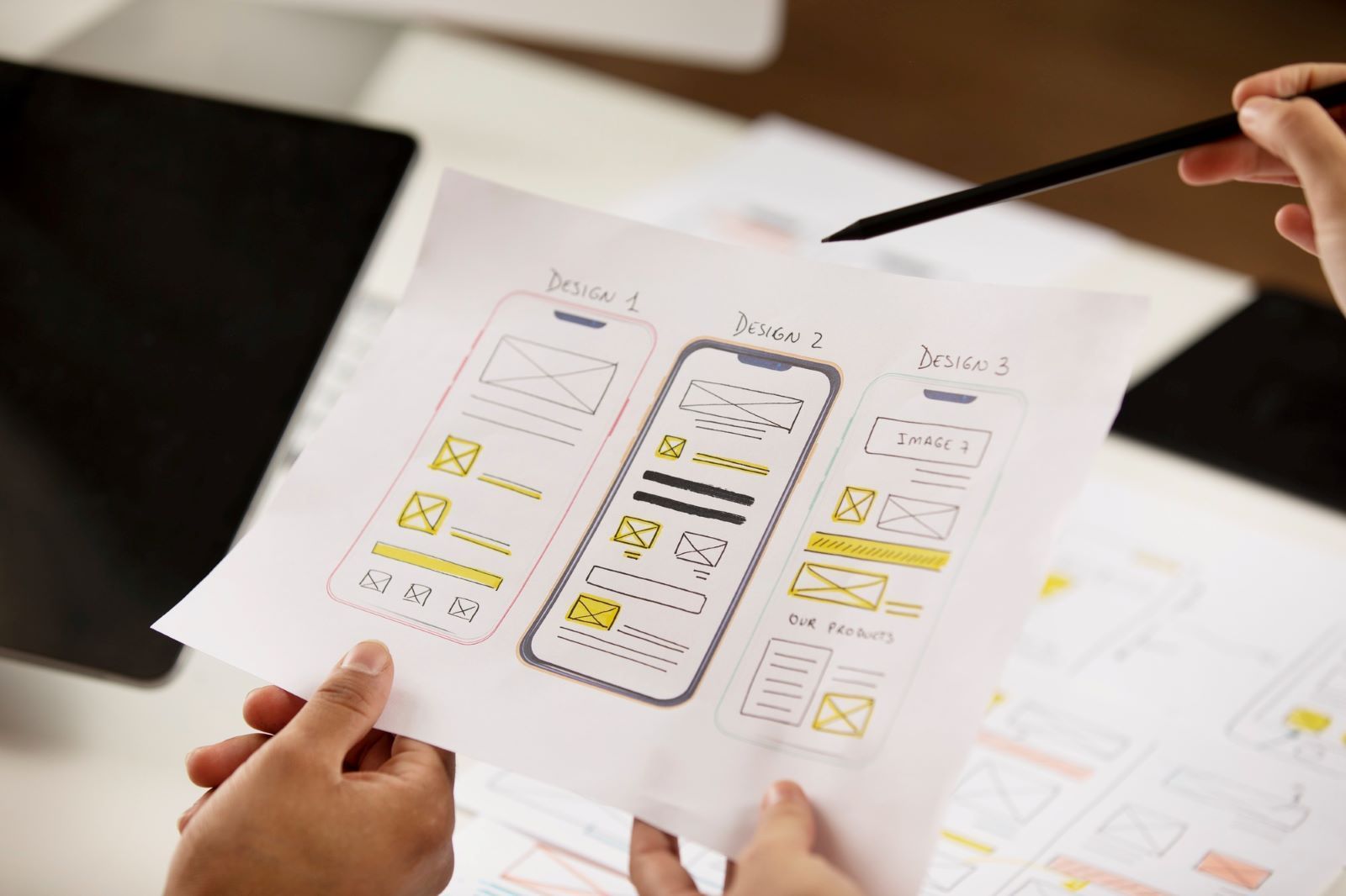 A person is holding a piece of paper with wireframes for a mobile app.