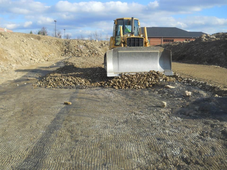 Bulldozer pushing rocks over a grid-like material on a construction site.