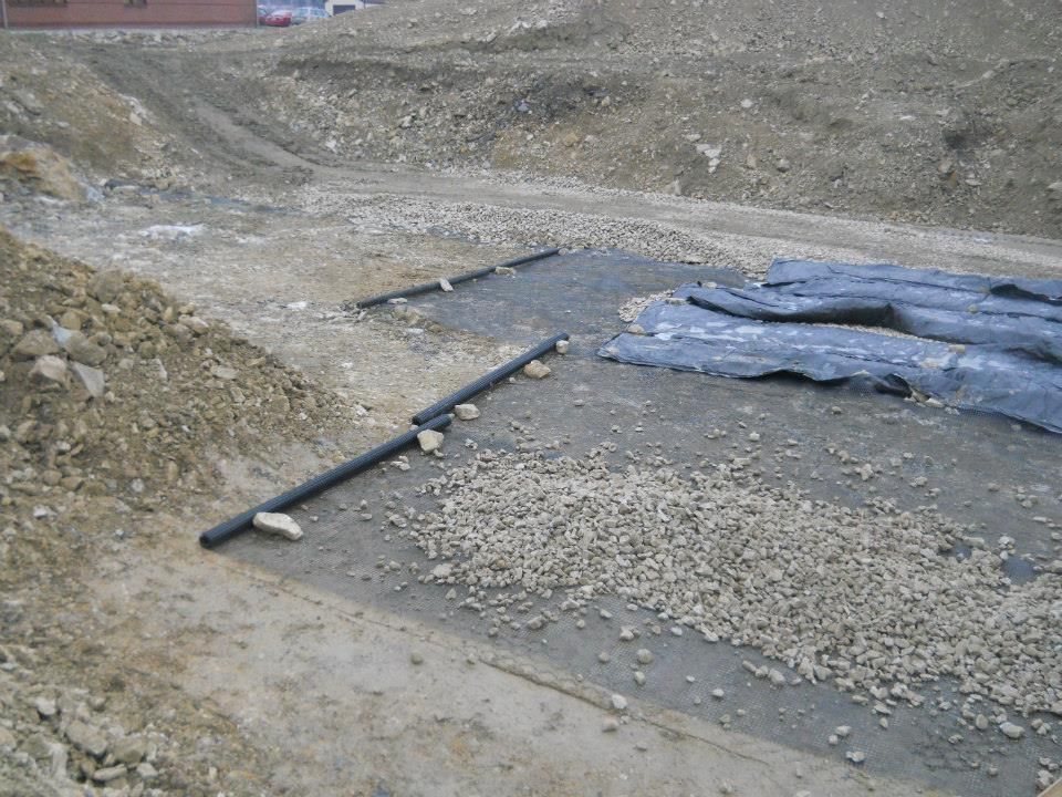 Construction site with drainage pipes, gravel, and protective sheeting.