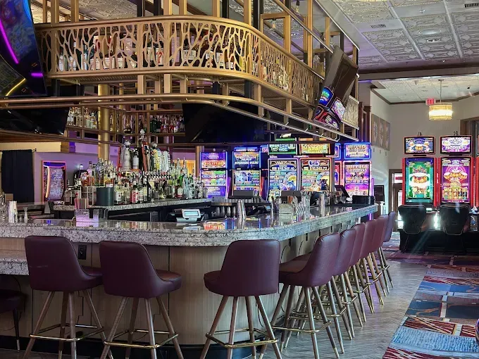 Bar with stools, slot machines, and upper-level seating. Gold accents and purple chairs.