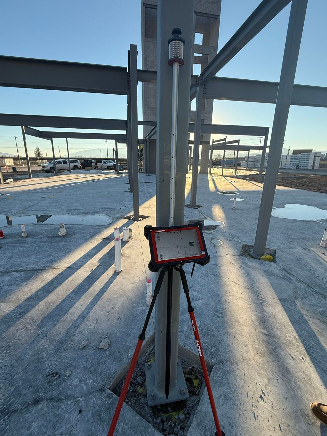 A construction site with a survey setup. A tablet on a tripod is near a steel beam.