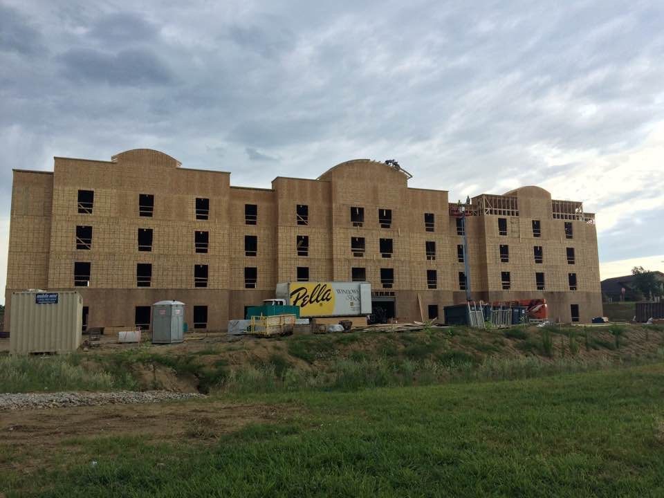 Building under construction; wood frame with many window openings, cloudy sky.