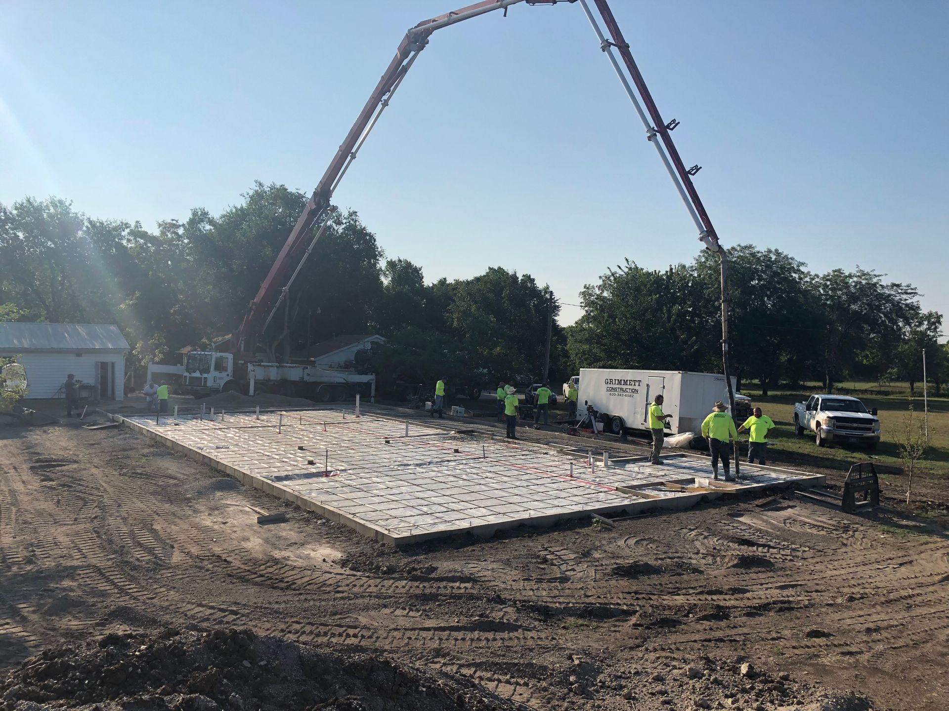 Construction workers pouring concrete for a foundation, using a pump truck. Sunny day.