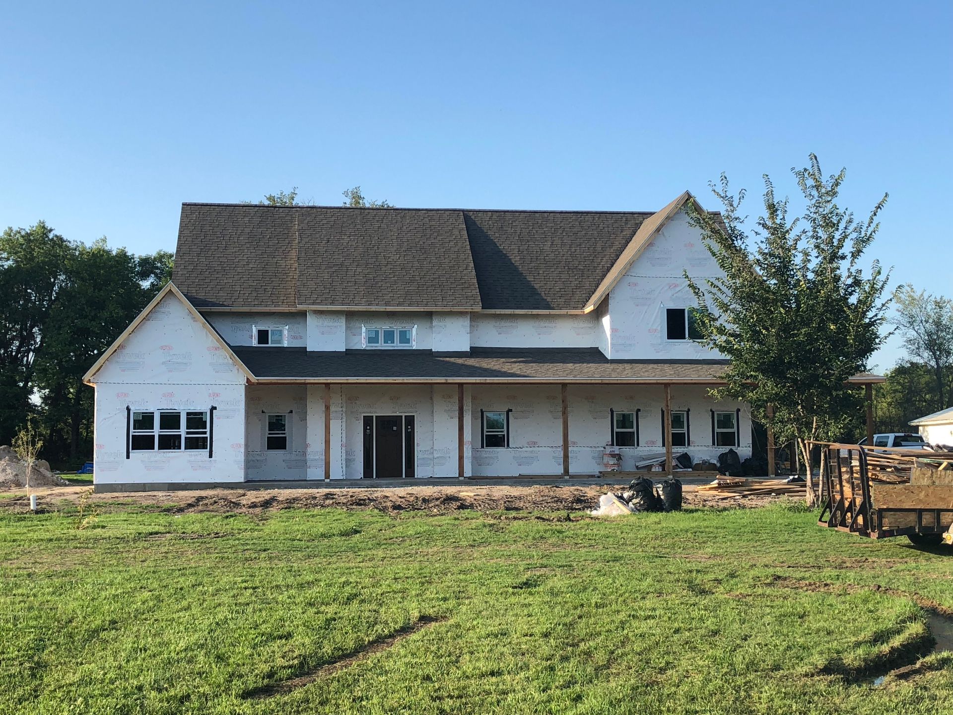 House under construction with grey roof, white siding, and porch in a grassy field.