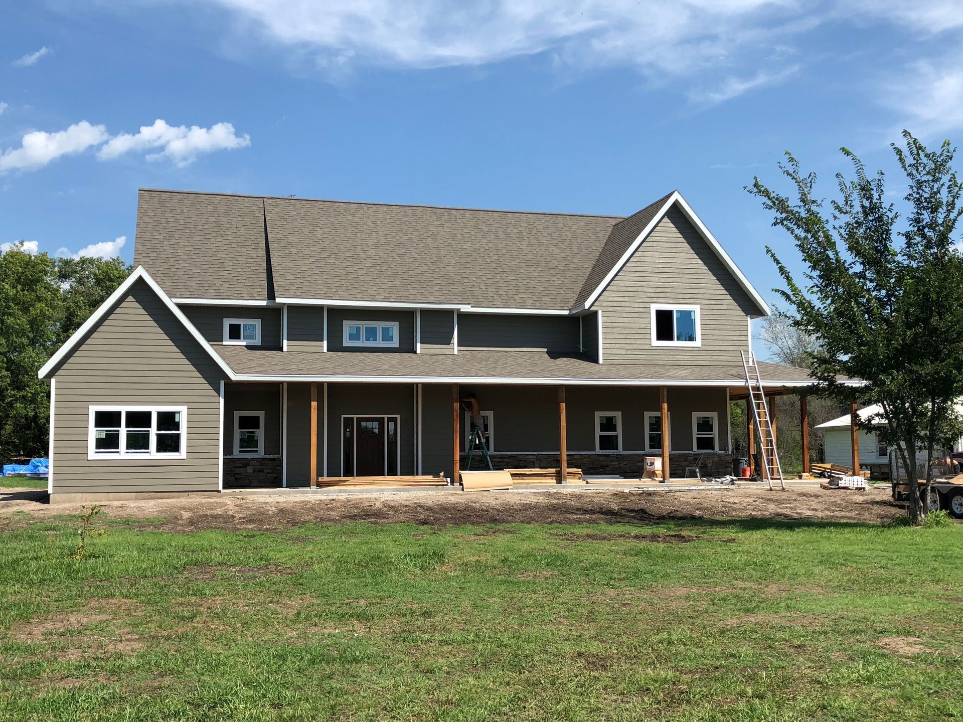 Two-story house under construction with gray siding and brown columns on a sunny day.