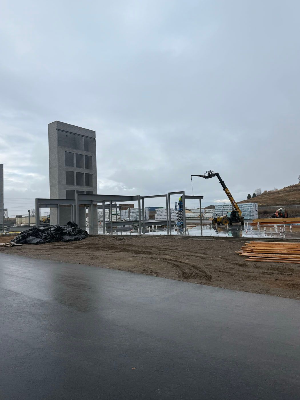 Construction site with steel framework and concrete tower under overcast sky.