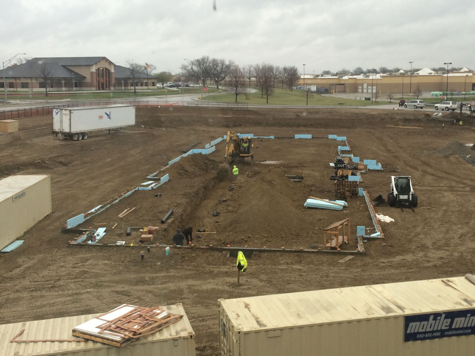 Construction site: Excavation for a building foundation with heavy machinery, surrounding dirt, and containers.