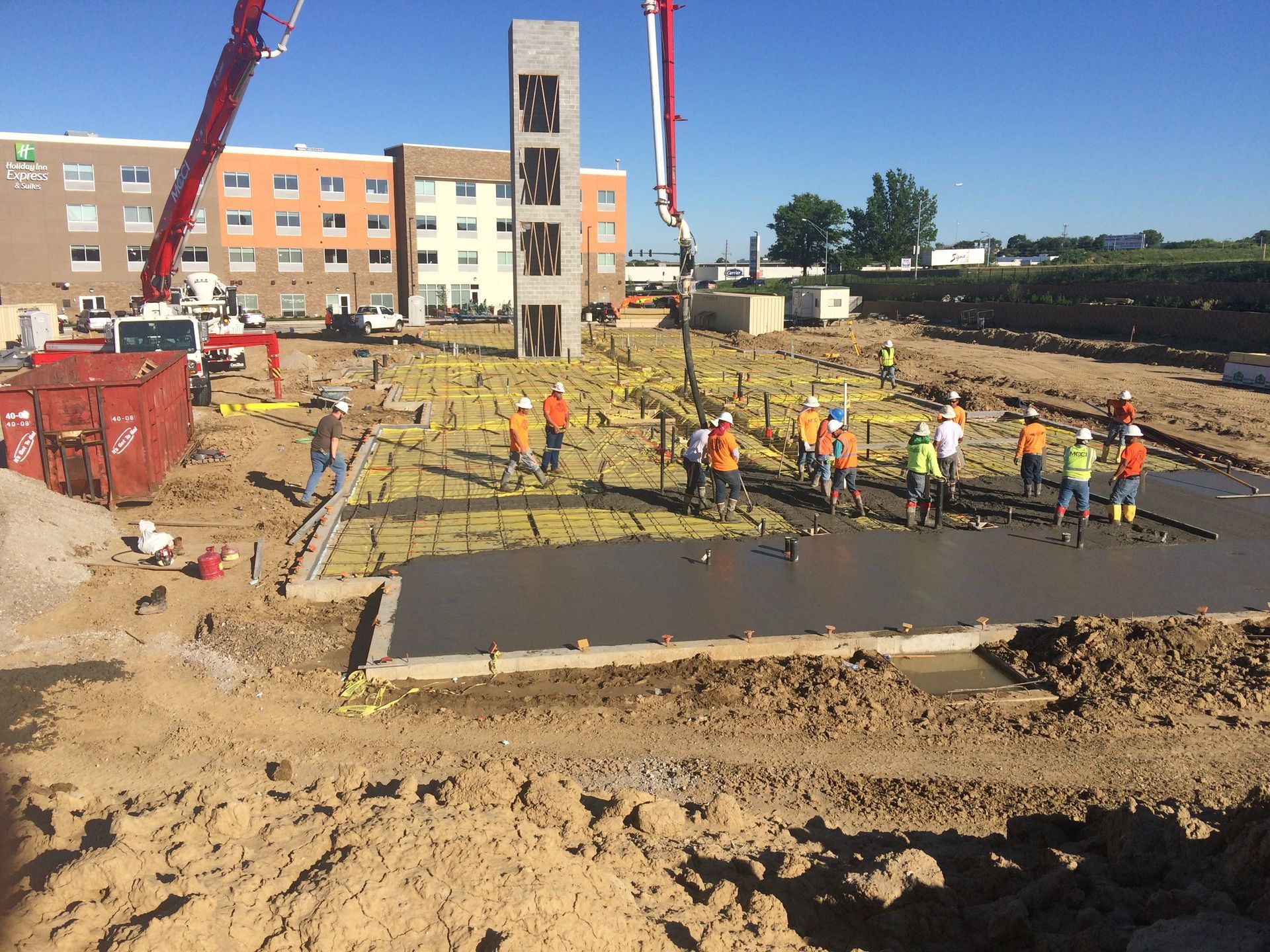 Construction site with workers pouring concrete; Holiday Inn in background; concrete pump truck.