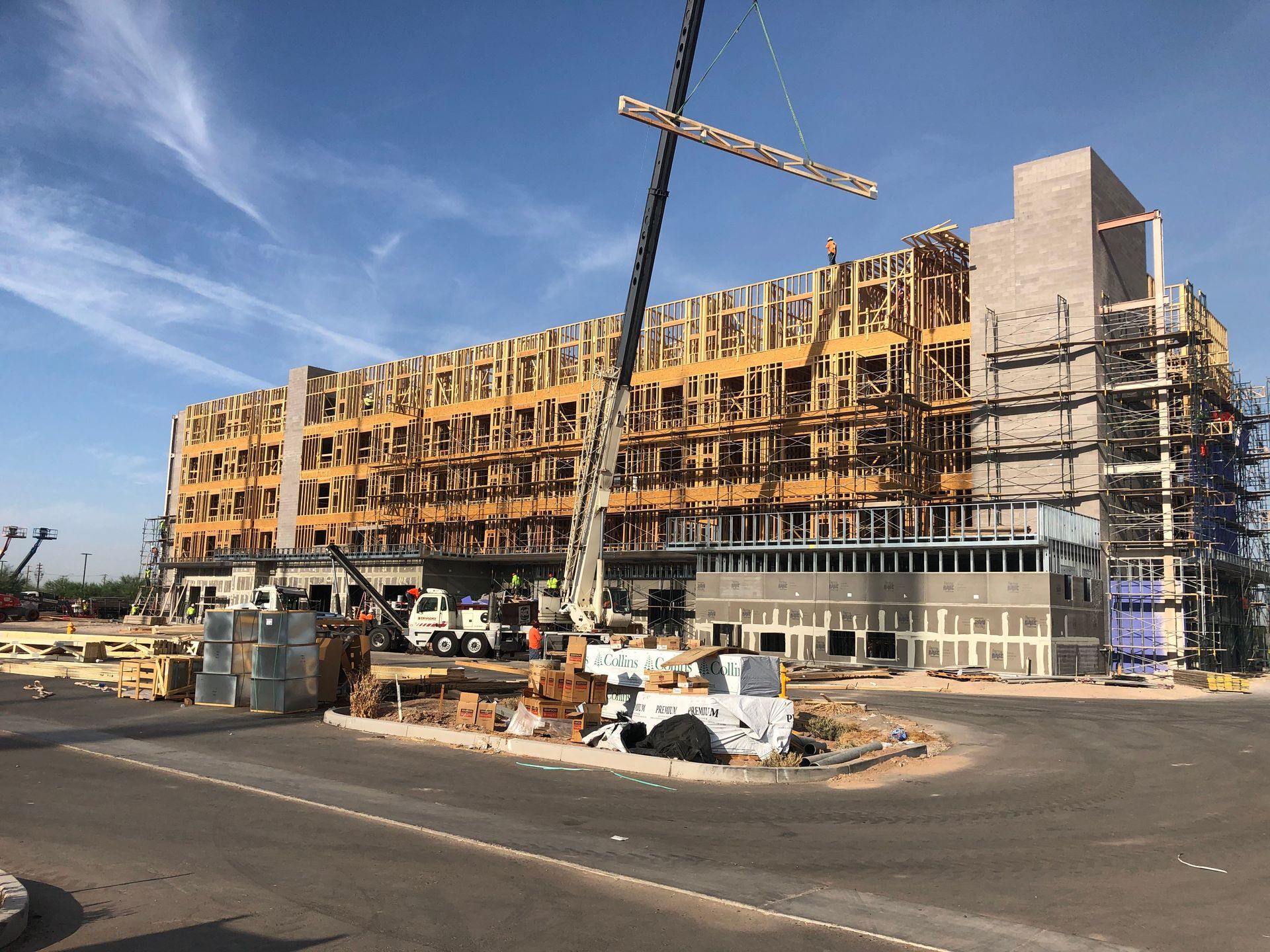 Building under construction with wooden frame, crane, scaffolding, and workers. Blue sky.