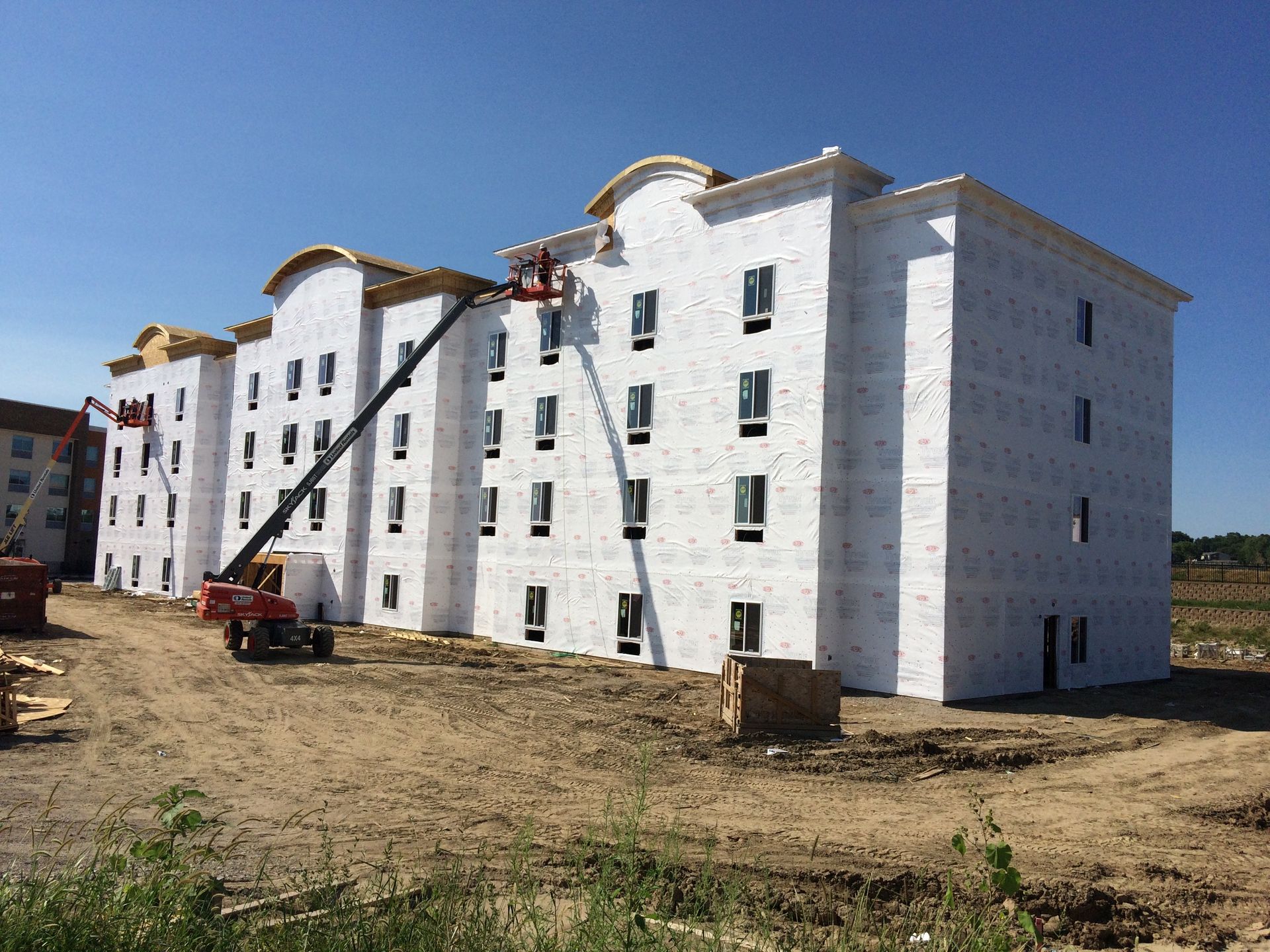 Multi-story building under construction, wrapped in white material, with two lifts and workers.
